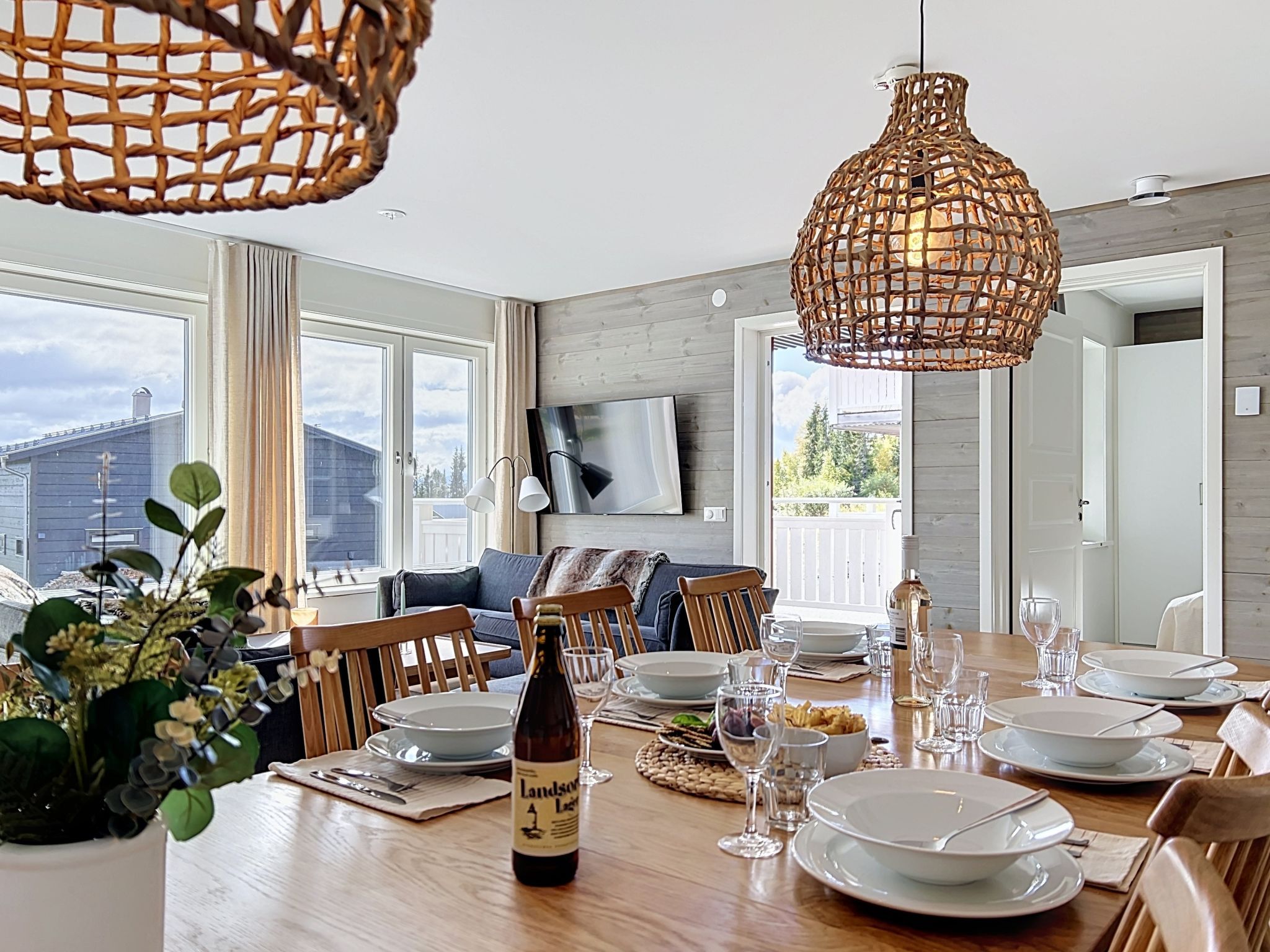 A dining area with a wooden table set for a meal, a bottle of wine, and a woven pendant light.