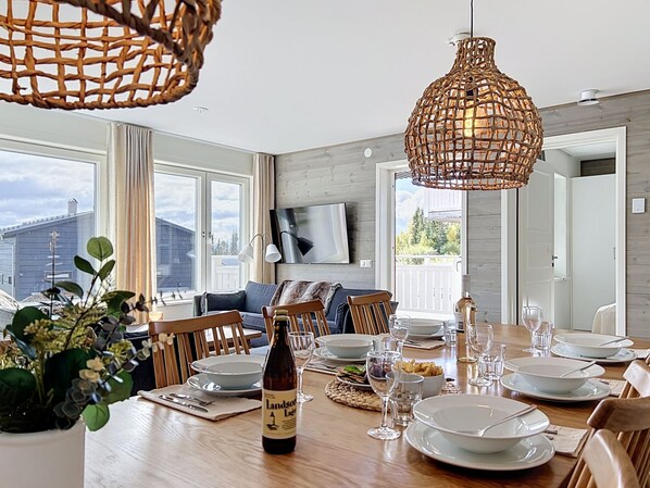A dining area with a wooden table set for a meal, a bottle of wine, and a woven pendant light.