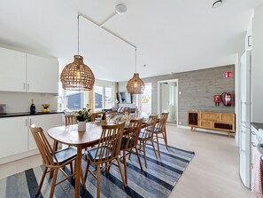 A modern kitchen with white cabinets, a dining area with wooden chairs and a round table, and a large window providing natural light. - Trillevallen 4 by Interhome (Trillevallen)