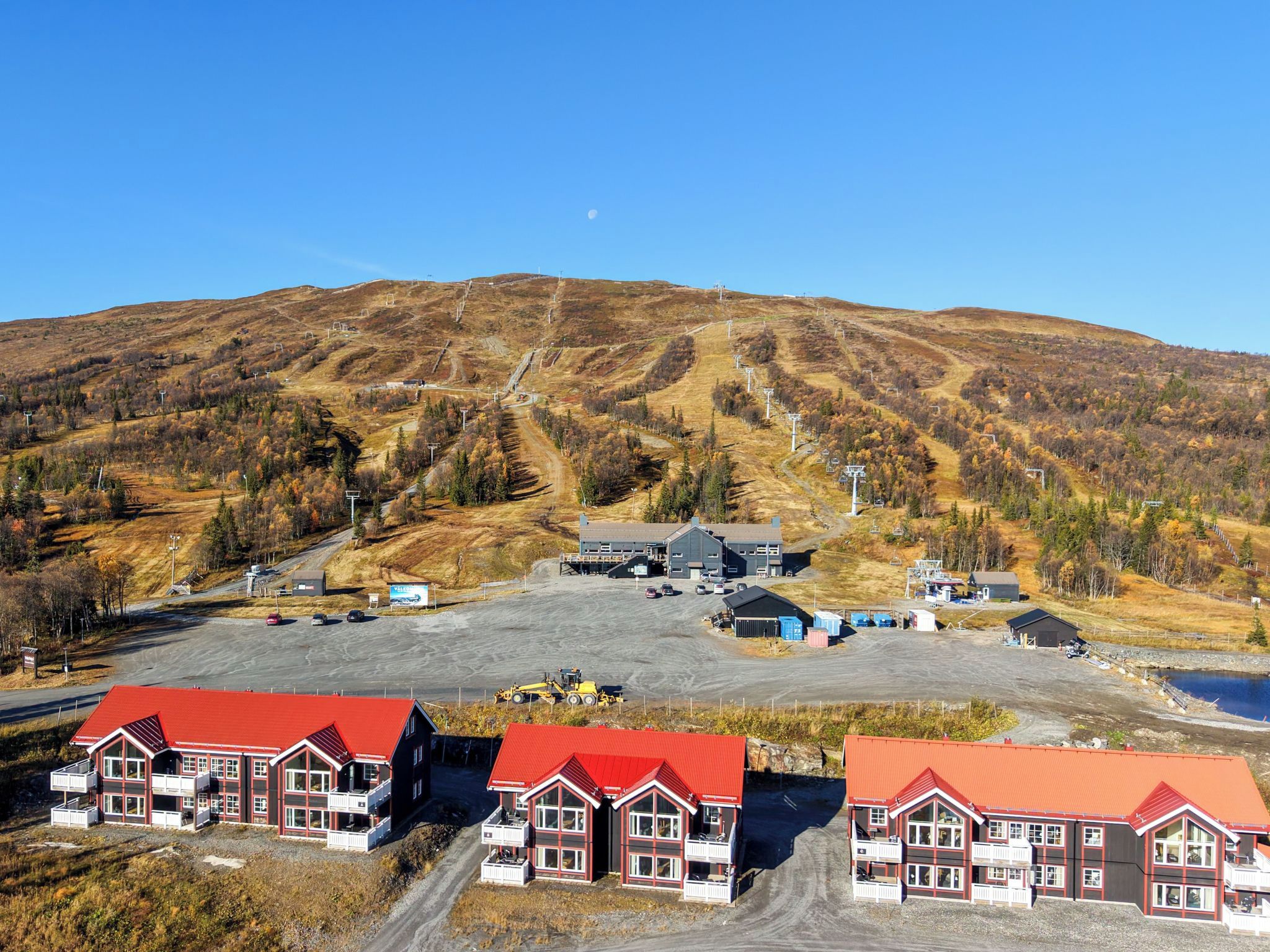 Ett bergigt landskap med en skidlift, en parkeringsplats och byggnader med röda tak.