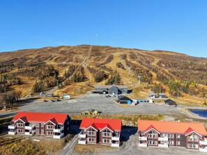 Et bjergrigt landskab med en gondolbane, en parkeringsplads og bygninger med røde tage.