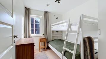 Ett sovrum med våningssängar, ett skrivbord, en stol och ett fönster med gardiner.