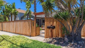 A wooden fence with a mailbox, a palm tree, and a house in the background. - Walk to the beach! The Moonlight Beach Bungalow (Encinitas)
