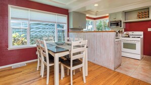 A modern kitchen with white cabinets, a central island, and a dining area with a table and chairs. - Walk to the beach! The Moonlight Beach Bungalow (Encinitas)