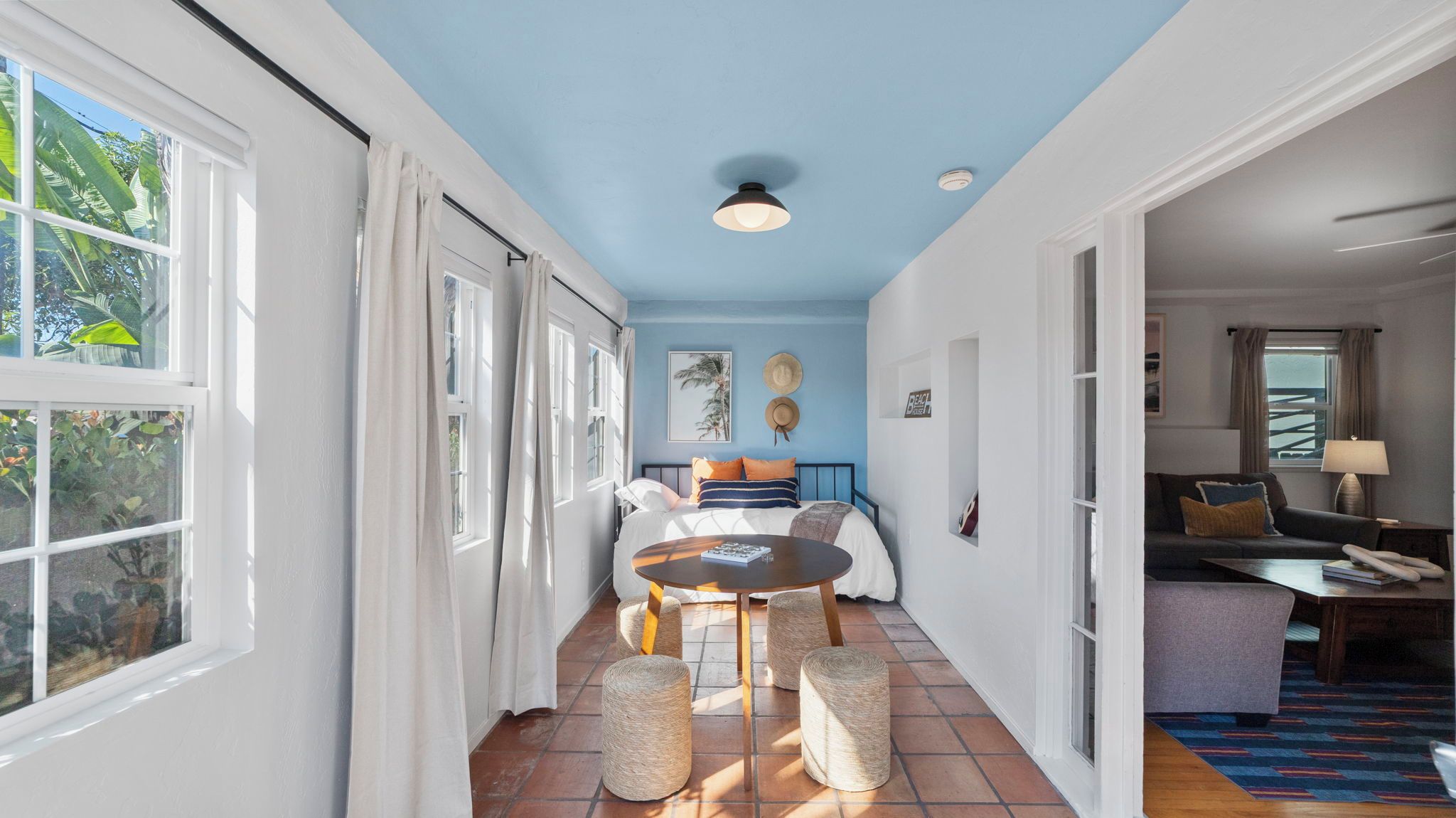 A bright room with a blue ceiling, a round table with chairs, and a bed with pillows.