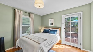 Un dormitorio con cama, ventana con cortinas, puerta hacia el exterior y una lámpara en el techo.