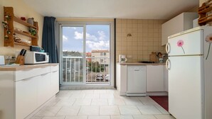 Una cocina compacta equipada con microondas, cafetera y refrigerador. Hay una puerta corrediza de vidrio que da a un balcón con vistas a edificios y coches aparcados.