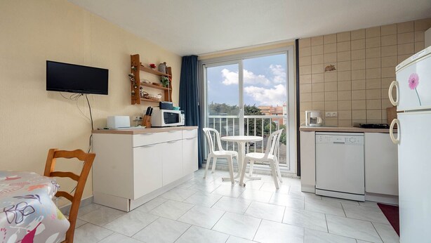 Una cocina compacta equipada con microondas, cafetera y refrigerador. Hay una mesa de comedor con sillas y un televisor montado en la pared.