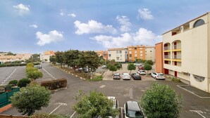 Un estacionamiento con coches, árboles y edificios al fondo.