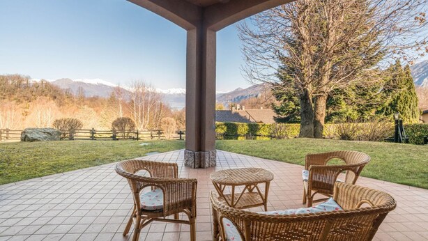 Eine überdachte Terrasse mit Korbmöbeln und Blick auf die Berge.