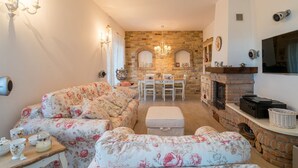 Ein gemütliches Wohnzimmer mit einer blumigen Couch, einem Kamin und einem Essbereich mit Tisch und Stühlen.