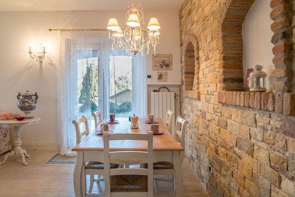 A dining area with a wooden table, white chairs, a chandelier, and a brick wall.