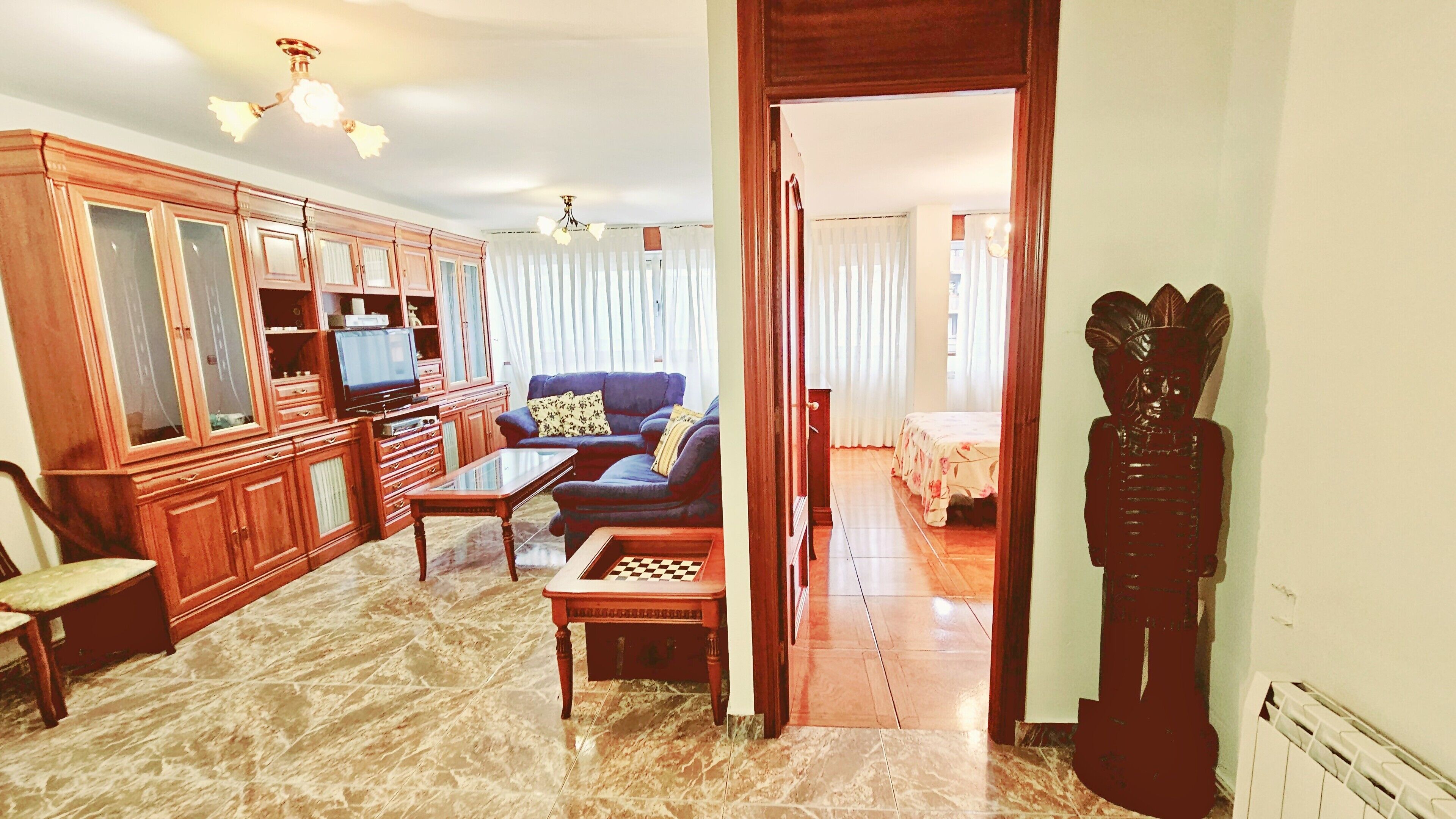 Una sala de estar con sofá, televisión, armarios de madera y un tablero de ajedrez.