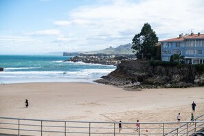 A beach with a rocky breakwater, a building with multiple windows, and a clear sky.