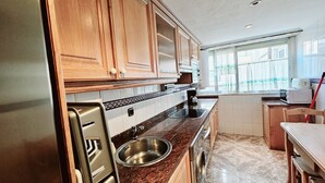 Cucina con mobili in legno, lavello in acciaio inossidabile, forno integrato e finestra con tende.