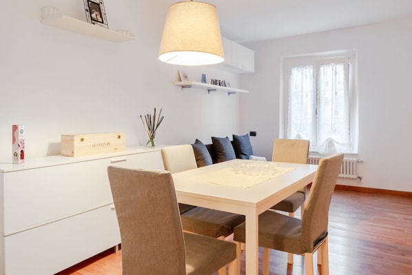 A dining area with a table, chairs, a hanging lamp, a sofa, and a window with curtains.