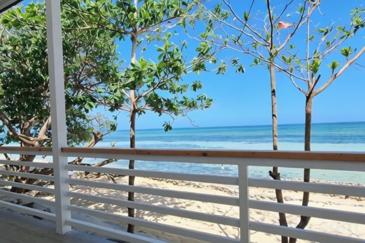 A beach view with a wooden railing, trees, and clear blue sky.
