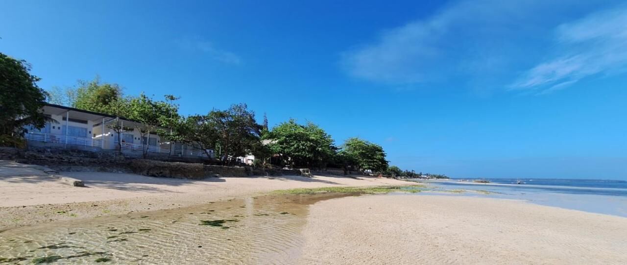 Une plage avec un bâtiment sur la gauche, un ciel dégagé et une eau calme.