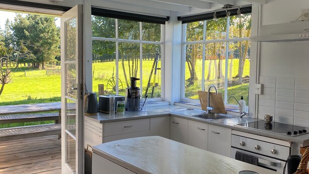 Una cocina moderna con amplios ventanales, techo de madera y vistas a un campo verde.