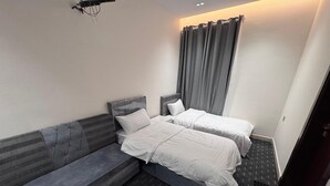Una habitación de hotel moderna con un sofá gris, dos camas individuales y un ventanal con cortinas grises.