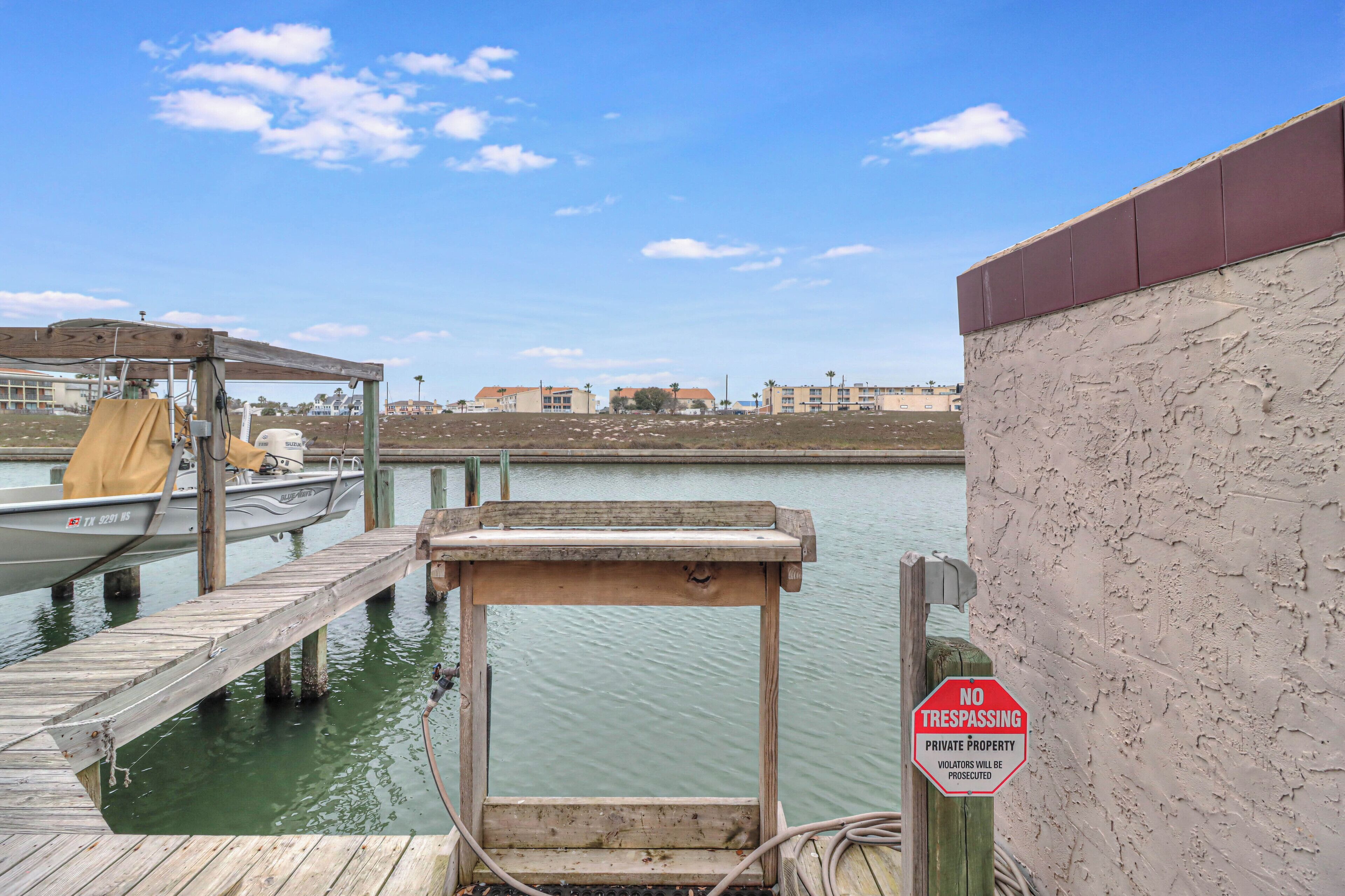 A wooden dock extending into calm water, a boat docked at the pier, and a 'No Trespassing' sign on a wall.