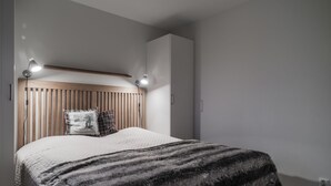 A bedroom with a wooden slatted headboard, a large bed with a patterned blanket, two bedside lamps, and a wardrobe.
