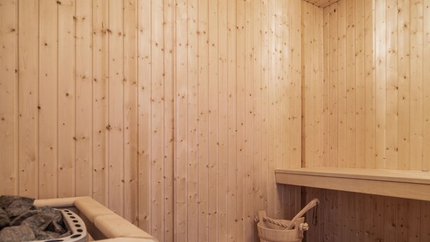 A sauna room with wooden walls, a bench, a bucket, and a heating element.
