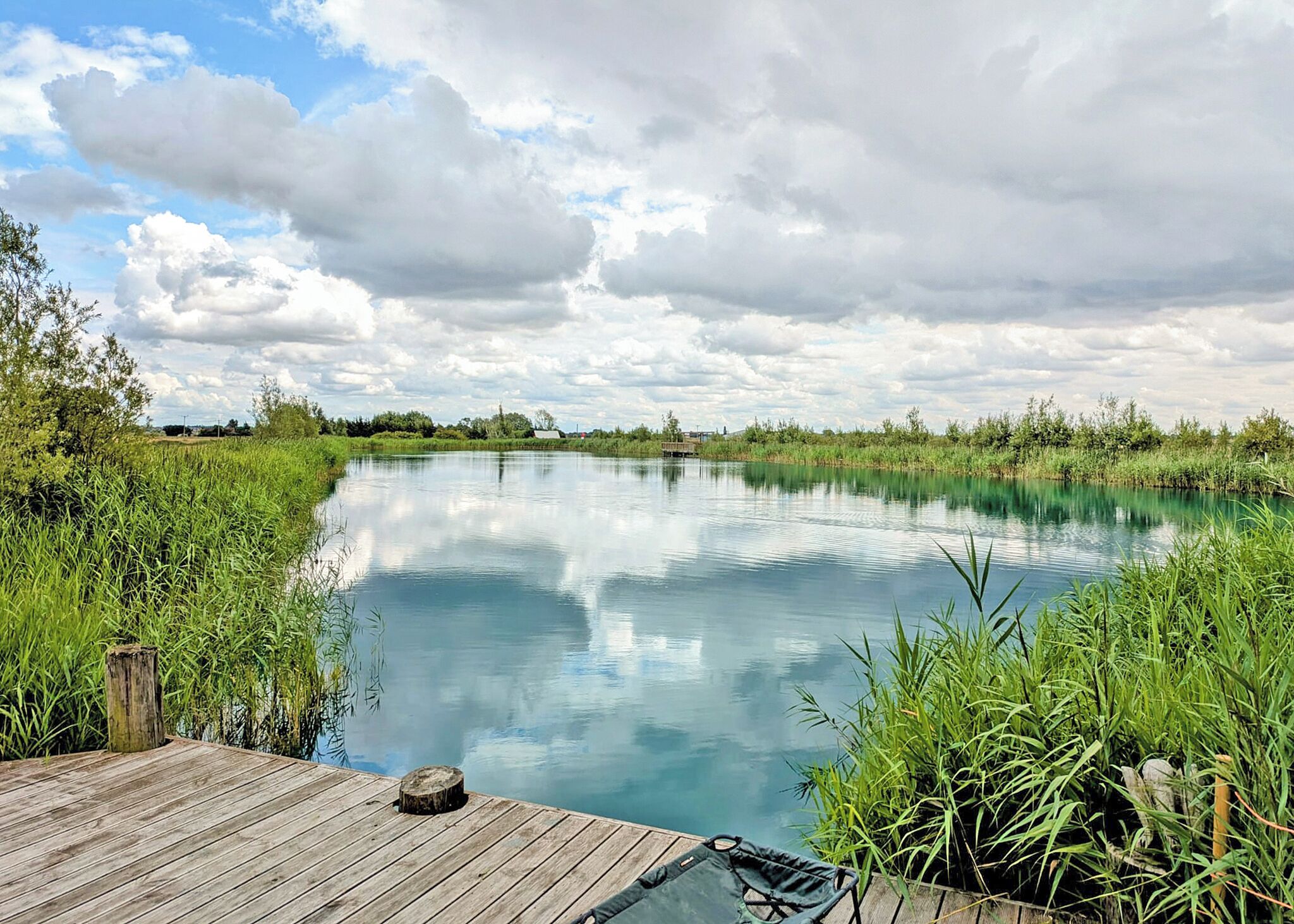 A calm river with a wooden dock and surrounding greenery.