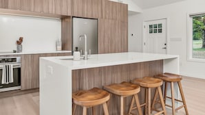 Eine moderne Küche mit einer zentralen Kochinsel, Holzbarhocker, einem eingebauten Ofen und einem großen Fenster.