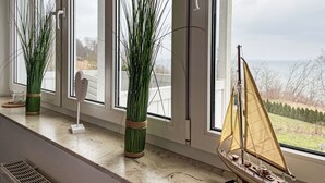 Una habitación con ventanas amplias, un velero en miniatura y plantas verdes altas.
