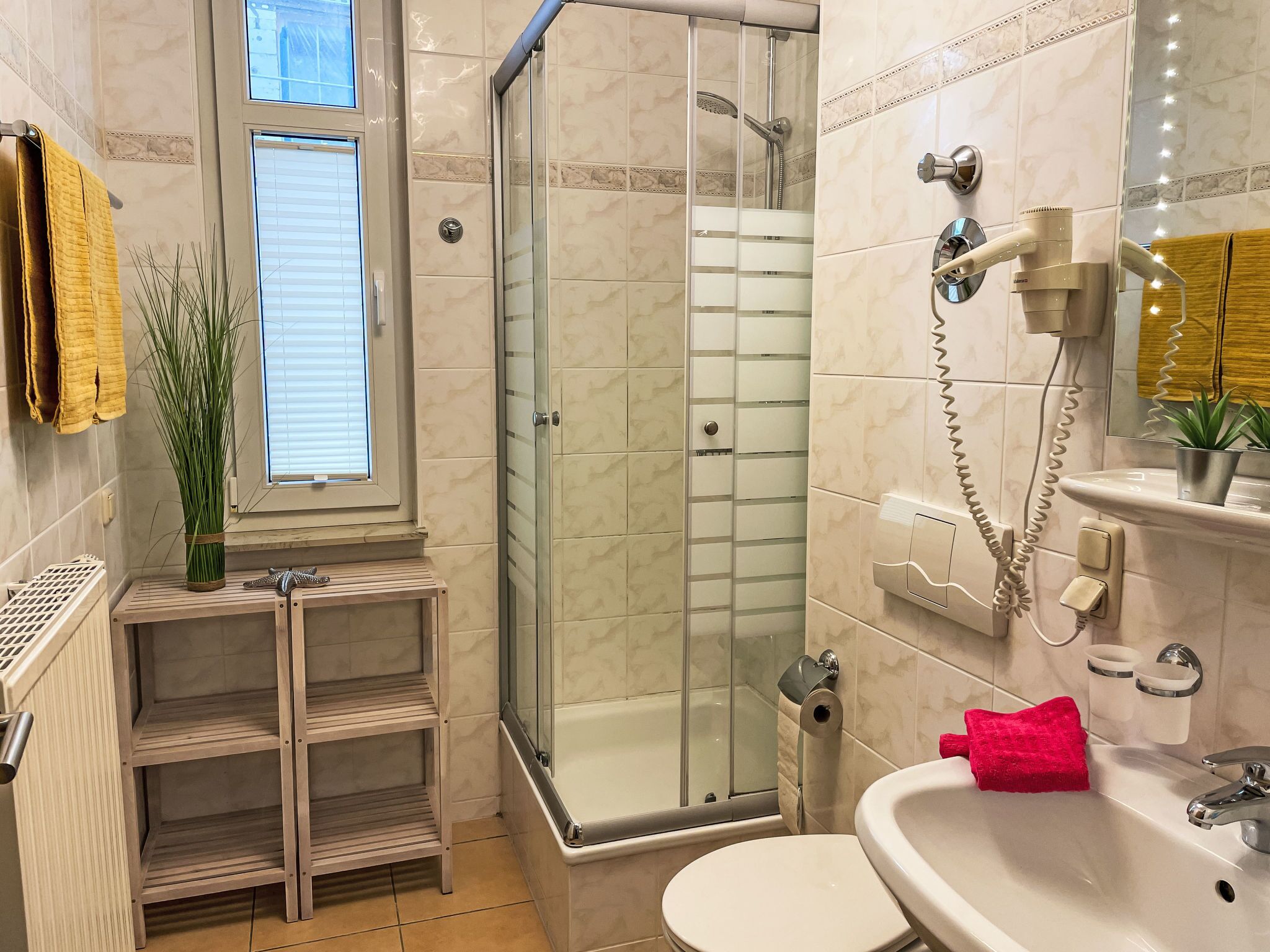 Ein Badezimmer mit Duschkabine, Toilette, Waschbecken und Spiegel sowie einem Fenster.
