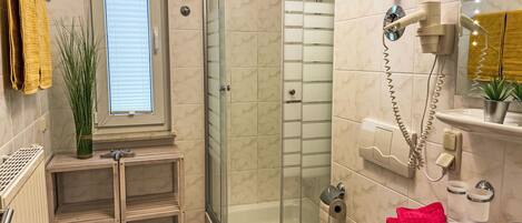 Ein Badezimmer mit Duschkabine, Toilette, Waschbecken und Spiegel sowie einem Fenster.