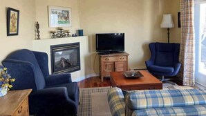 A living room with a television, two blue armchairs, a sofa, a fireplace, and a window with curtains.