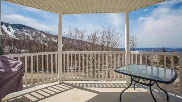 A covered outdoor area with a glass table and white railing, overlooking a snowy landscape.