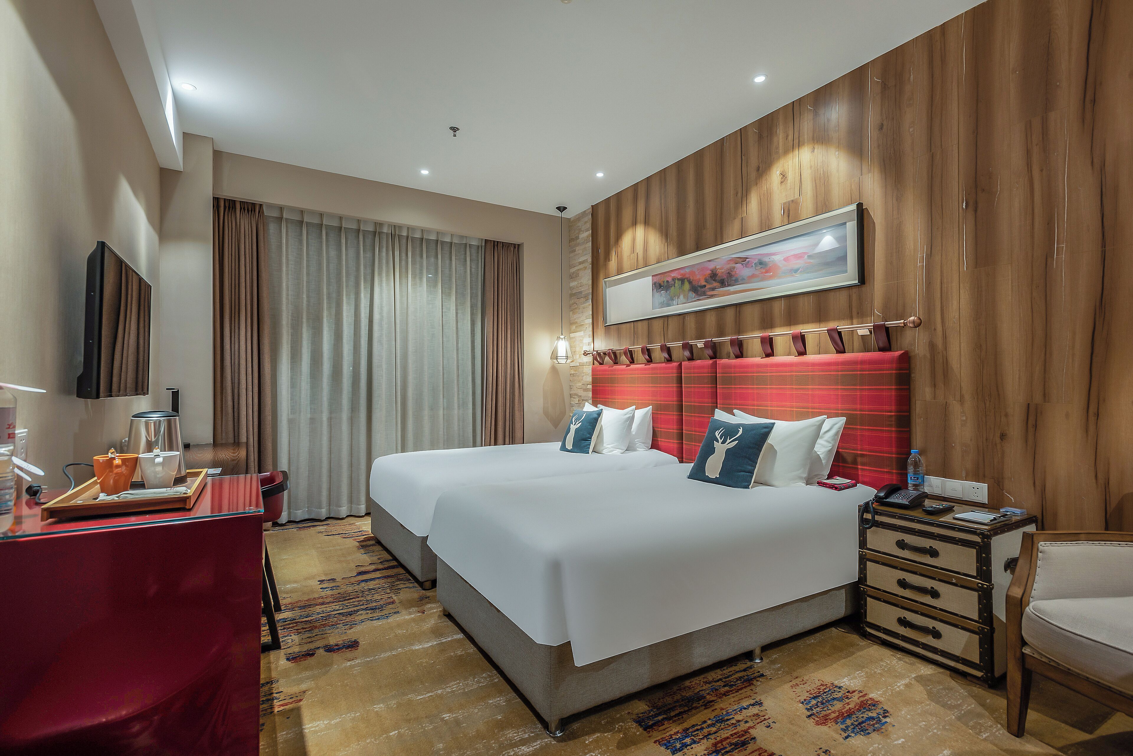 A hotel room with two beds, a desk with a coffee maker, a telephone, and a painting on the wall.