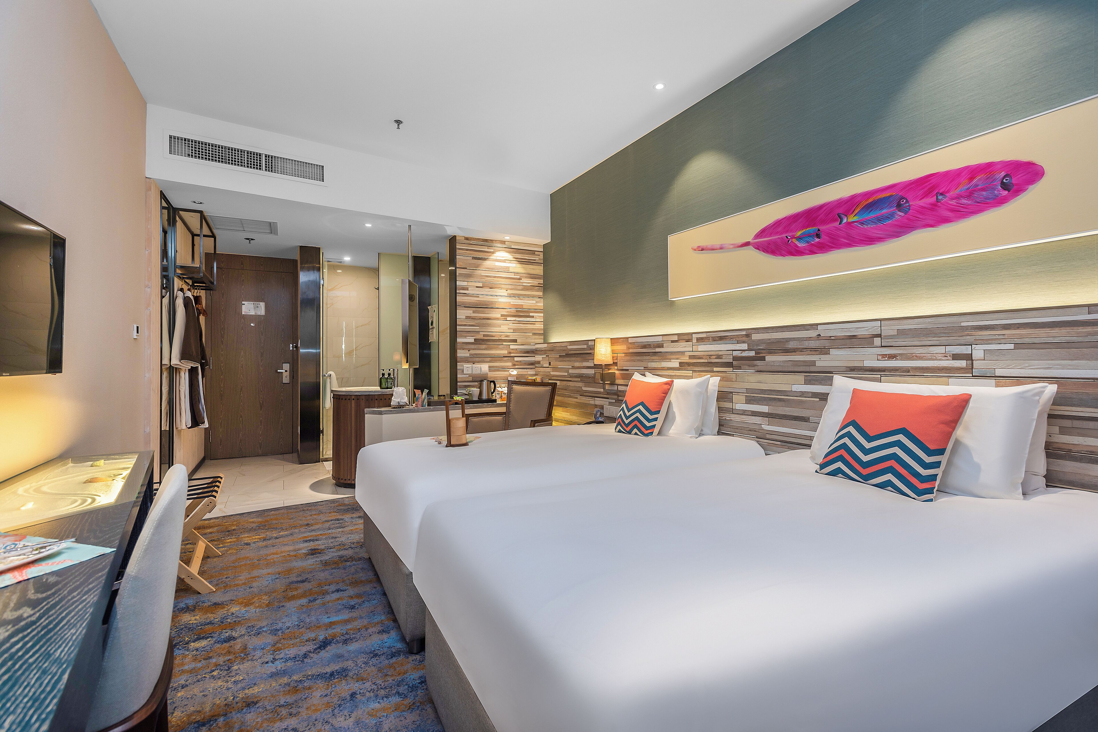 Une chambre d’hôtel avec un grand lit, un bureau et une chaise. Il y a un tableau accroché au mur, au-dessus du lit.