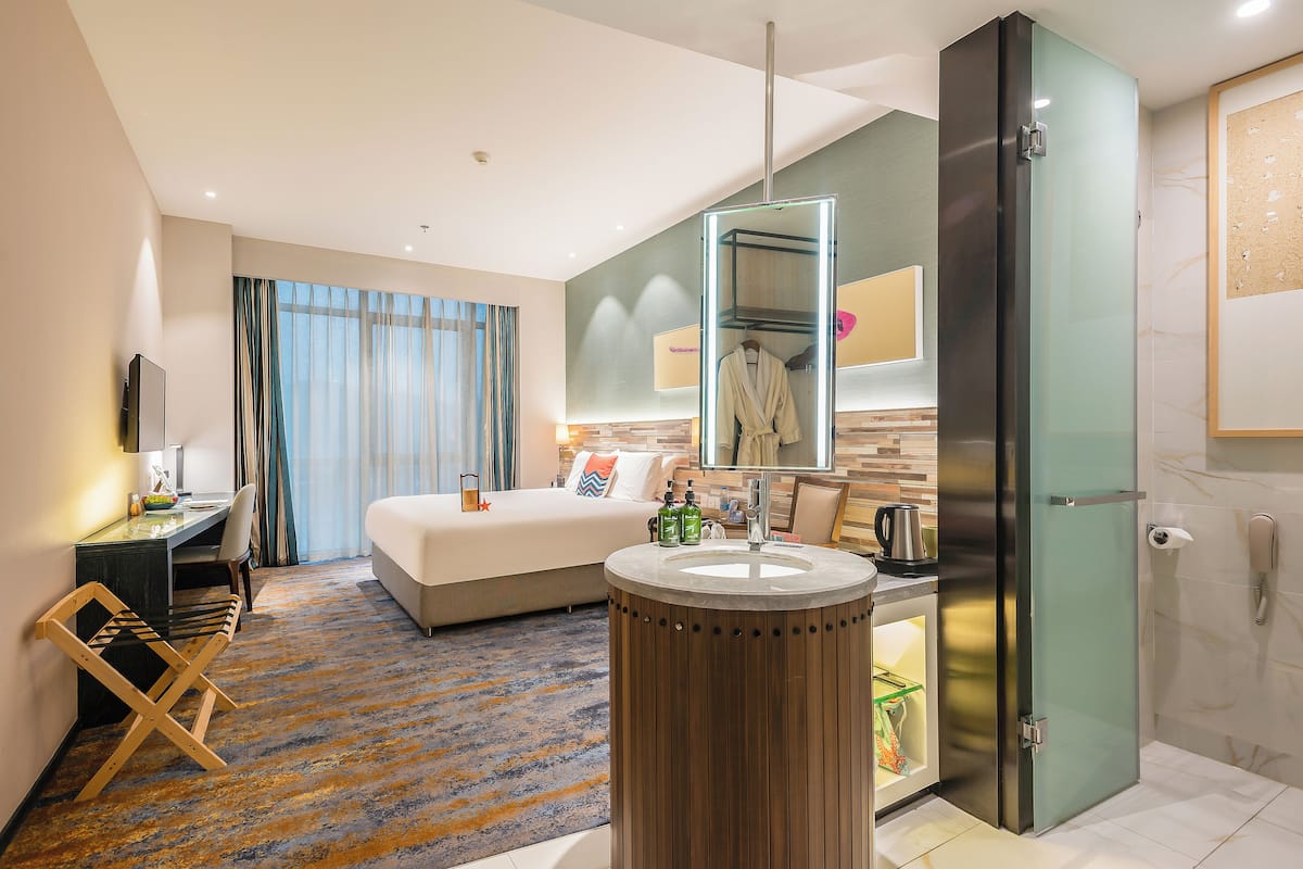 Habitación de hotel moderna con cama, escritorio, lavamanos redondo y espejo.