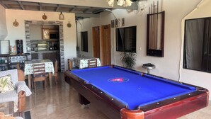 Une table de billard dans une pièce qui comprend un coin cuisine, une table à manger et un ventilateur de plafond.