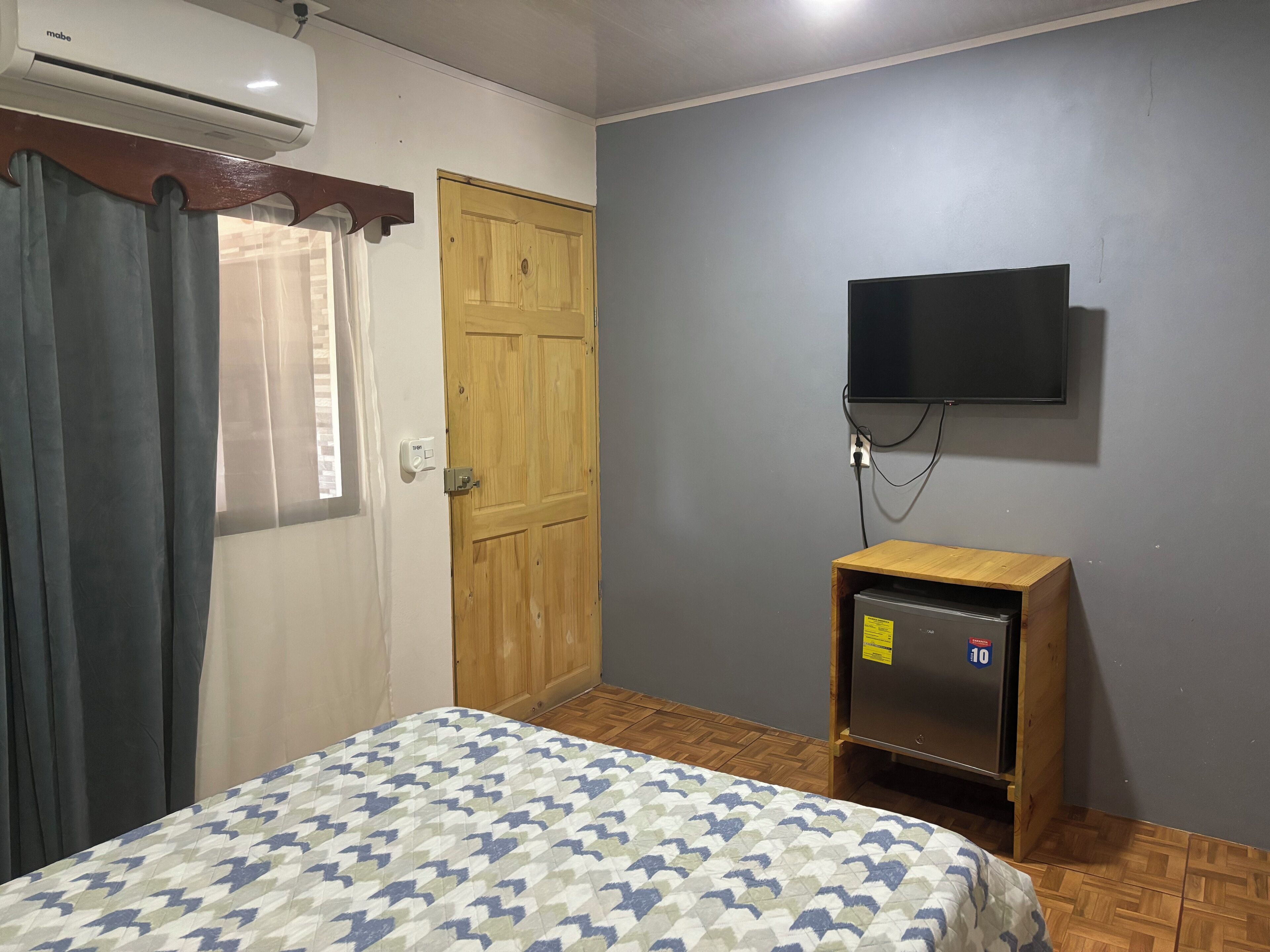 Un dormitorio con una cama, un armario de madera, un televisor montado en la pared y un equipo de aire acondicionado.
