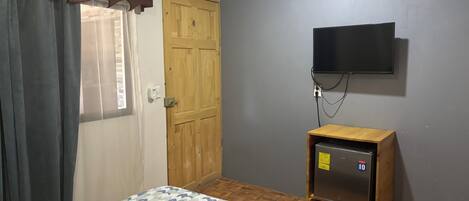Un dormitorio con una cama, un armario de madera, un televisor montado en la pared y un equipo de aire acondicionado.