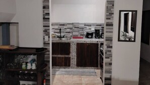 Une cuisine de taille réduite avec un plan de travail recouvert de carreaux, des meubles de rangement en bois foncé, une machine à café et un évier.