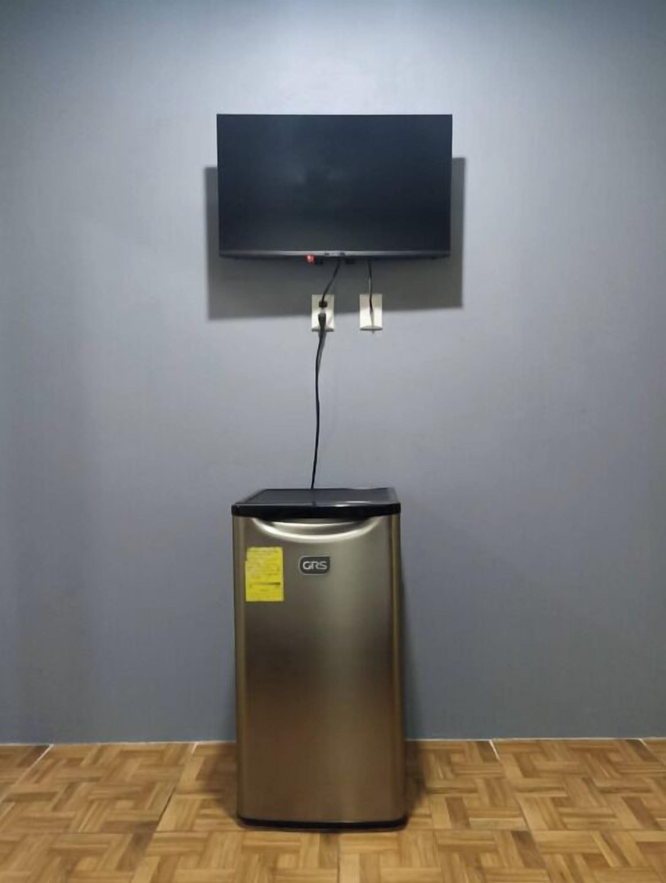 A room with a flat-screen TV mounted on the wall, a small metallic cabinet below it, and a wooden parquet floor.