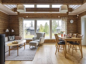 A cozy cabin interior with a dining area, a sofa, and a large window offering a view of the outdoors.