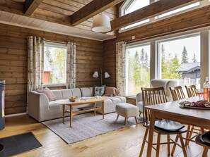 A cozy cabin interior with a sofa, dining table, and chairs, wooden walls, and large windows. - Trillevallen 601 by Interhome (Trillevallen)