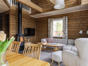 A cozy cabin interior with a fireplace, wooden walls, a sofa, and a dining area. - Trillevallen 601 by Interhome (Trillevallen)