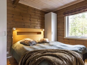 A wooden cabin bedroom with a bed, pillows, and a window. - Trillevallen 601 by Interhome (Trillevallen)