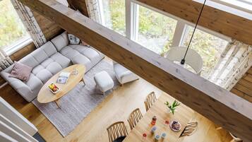 Un loft spacieux avec de hauts plafonds, un coin salon confortable, une table à manger où est dressé un repas, et de grandes fenêtres offrant une vue sur la verdure.