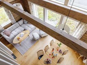 Un loft espacioso con techo alto, una zona de estar acogedora, una mesa de comedor con comida y ventanas grandes que ofrecen vistas a zonas verdes.