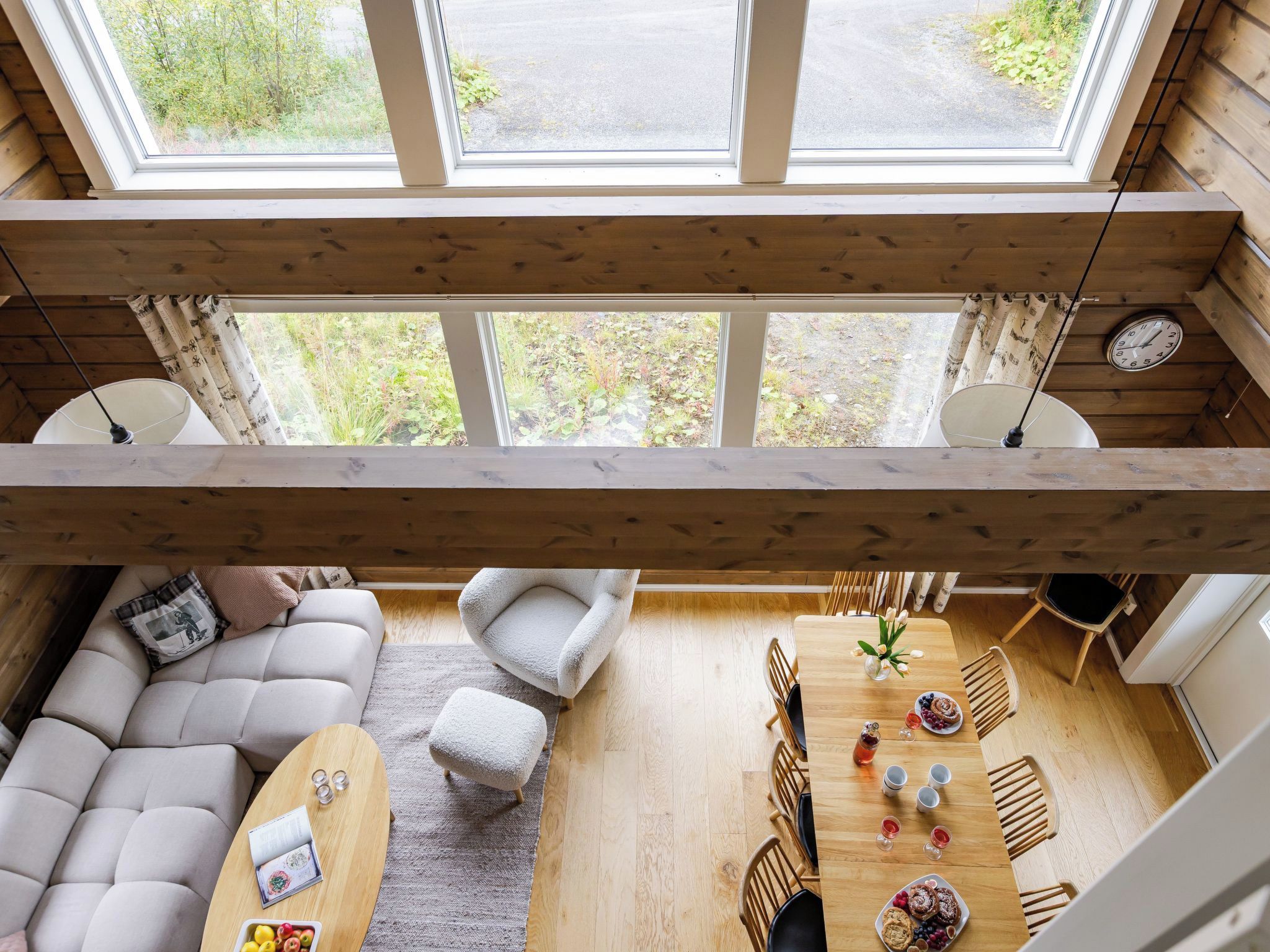 Une pièce aux hauts plafonds, avec un plafond en bois, un canapé, une table à manger avec des chaises, et une vue dégagée grâce à de grandes fenêtres.