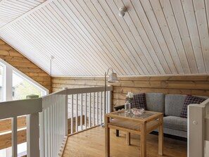 A wooden interior with a glass table, a sofa, and a white railing.